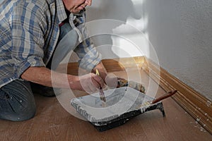 Close-up portrait of a builder worker decorator painting wall indoors in white color using roller, brush