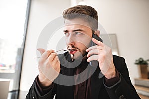 Close up portrait of a business man sitting in a light cafe, talking on the phone, eating a food fork and looking away