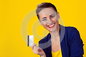 Close up portrait business woman with credit card smiling looking at camera you red lips  short hair boy alike isolated yellow