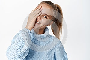 Close up portrait of carefree little girl, teen in winter sweater, touches her face and smiles, laughs and looks happy