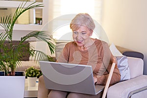 Close-up portrait of casual senior woman using her laptop while sitting on couch and working. Attractive middle aged businesswoman