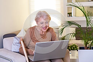 Close-up portrait of casual senior woman using her laptop while sitting on couch and working. Attractive middle aged businesswoman