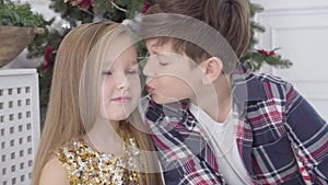 Close-up portrait of Caucasian boy kissing cute girl on cheek under Christmas tree. New Year`s eve, first love