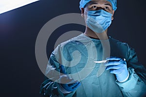 Close-up portrait of a caucasian doctor surgeon, in a sterile suit, mask, holding a scalpel in his hands, preparing to operate. On