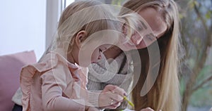 Close-up portrait of Caucasian mother and baby girl sitting at home and drawing with colorful pencils. Young smiling