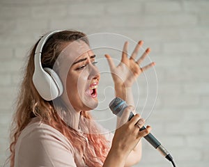 Close-up portrait of a caucasian woman with curly hair singing into a microphone. Beautiful emotional girl in white