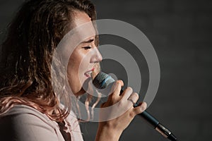 Close-up portrait of a caucasian woman with curly hair singing into a microphone. Beautiful sensual blonde girl is