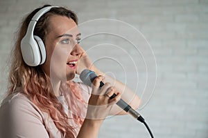 Close-up portrait of a caucasian woman with curly hair singing into a microphone. Beautiful sensual girl in white