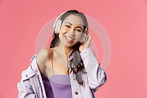 Close-up portrait of charismatic good-looking korean girl enjoying listening music, wear headphones smiling and dancing