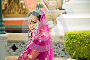 Close up portrait charming Asian woman wearing a purple Indian traditional saree with a wall in Buddhist templ background