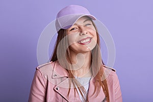 Close up portrait of charming beautiful young female smiling sincerely, being in good mood, standing isolated over lilac