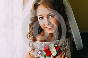 Close-up portrait of charming bride in wedding dress holding a cute bouquet with red and white roses