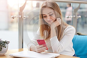 Close up portrait of charming female using mobile phone during break between lectures in coffee shop, young student holding her