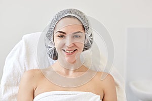 Close up portrait of charming good looking female posing over white wall in beauty parlor wearing medical cap and white towel,
