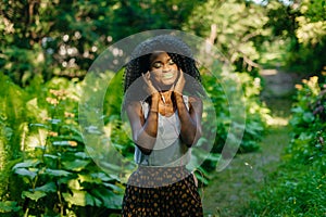 Close-up portrait of the charming peaceful african girl with green lipstick and eyeshadows putting the earphones at the