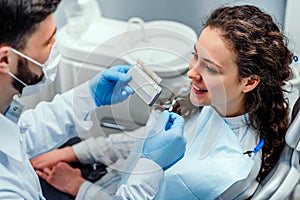 Close up portrait of charming young woman sitting in dental chair while stomatologist selecting color tone of her teeth
