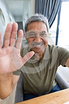 Close-up portrait of cheerful biracial senior man waving hand while talking over video call