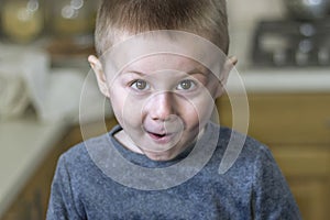 Close up portrait of cheerful emotional kid. Little boy makes faces in the kitchen at home.