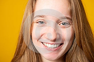 Close-up portrait of a cheerful girl. Studio portrait of a smiling teenage girl on a yellow background