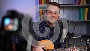 Close-up portrait of cheerful guitarist singer male playing acoustic guitar and singing song, recording video with