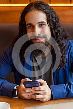 Close up portrait of cheerful handsome intelligence young adult man freelancer in casual style sitting in cafe, holding phone and