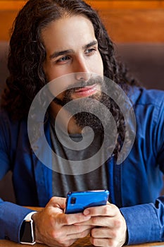 Close up portrait of cheerful handsome intelligence young adult man freelancer in casual style sitting in cafe, holding phone and