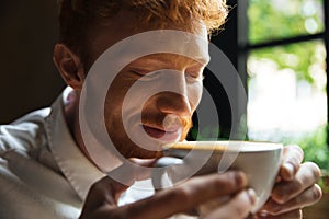 Close-up portrait of cheerful readhead bearded man sniffs coffee