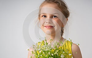 Close up portrait of a cheerful smiling little girl dressed in yellow holding bunch of field flowers in hands. Studio