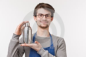 Close-up portrait of cheerful smiling young bartender working on inventing new cocktail, shaking drink in shaker and