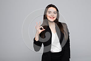 Close up portrait of a cheerful young business woman showing okay gesture isolated over gray background