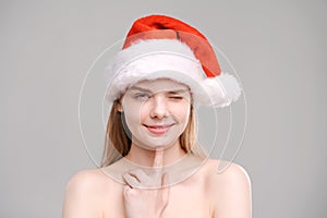 Close-up portrait cheerful young woman in red Santa Claus outfit touches her