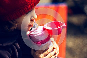 Close-up portrait of child girl drinking water from thermo bottle for kids.