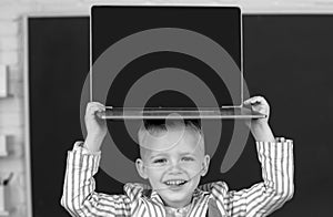 Close up portrait of child holding laptop on head, gadgets to study. Computer education for kids.