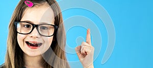 Close up portrait of a child school girl wearing looking glasses holding up point finger in I have an idea gesture isolated on