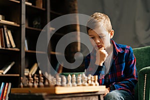 Close-up portrait of clever pensive little boy thinking about next move over the chessboard