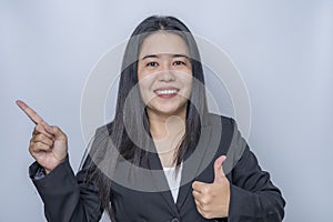 Close-up portrait of confident adult businesswoman showing thumb up with hand to presenting or pointing isolated on grey