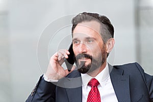 Close-up portrait of confident businessman dressed in suit talking on mobile phone isolated over gray background outside