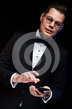 Close-up portrait of confident handsome elegant stylish businessman with bow-tie in glasses holding phone in his hands