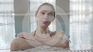 Close-up portrait of confident smiling woman posing at poolside. Attractive Caucasian brunette girl with brown eyes