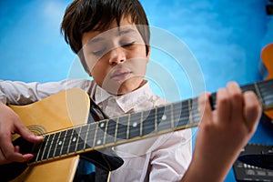 Close-up portrait of confident teenager boy plucking strings while strumming his guitar with delight. Inspired teenager