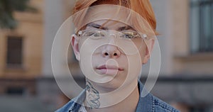 Close-up portrait of confident young Asian man student wearing stylish glasses looking at camera in city street