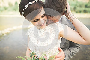 Close up portrait of couple against river and green trees. Beautiful young woman kissing handsome man outdoors