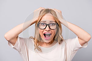 Close up portrait of crazy shocked woman in formal-wear and glasses touching her hair against gray background