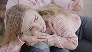 Close-up portrait of crying Caucasian girl lying on mother`s knees and talking. Teenage daughter sharing problems with