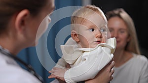 Close-up portrait of curios baby girl looking back at blurred mother as doctor talking to adorable charming child
