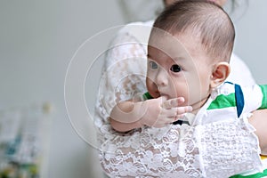 Close up portrait cut boy baby sucking his finger while mother carrying in bedroom. Relationship and love lifestyle mother`