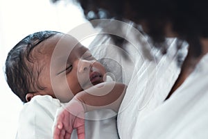 Close up portrait of cute African american newborn infant baby lying in mother's arms at hospital. Black Mother hand lulling