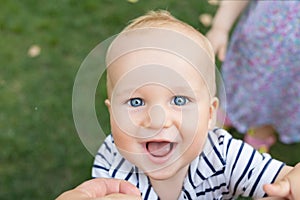 Close-up portrait of cute caucasian baby boy smiling and having fun with parents outdoors. Happy infant face with big