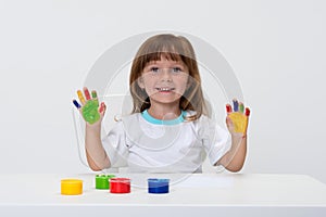 Close-up portrait of a cute cheerful happy smiling little girl draws her own hands with gouache or finger paints isolated on white