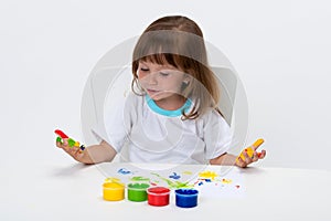 Close-up portrait of a cute cheerful happy smiling little girl draws her own hands with gouache or finger paints isolated on white